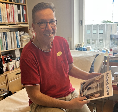 Boris Klanger sitter på ett skrivbord och tittar in i kameran med en tidning i händerna.